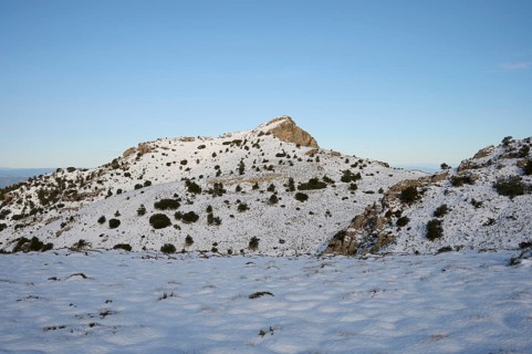 A serene winter scene at Montcabrer in Spain, showcasing its snow-capped peak under a clear blue