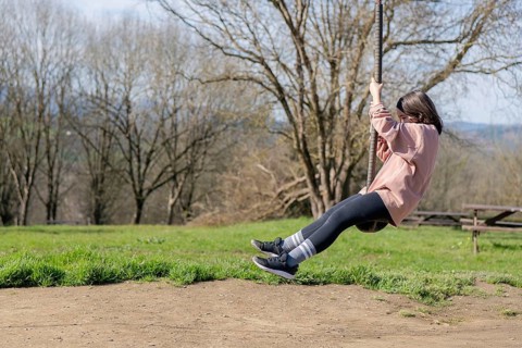A young girl enjoys a whimsical ride on a zip line in a sunny park. Her casual attire and the