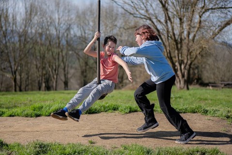 Two friends enjoy a sunny day by playing on a zip line in a park. Laughter and joy fill the air as