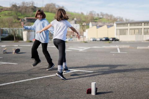 Two friends joyfully dance and play an outdoor game in an empty urban parking lot. Skateboards rest
