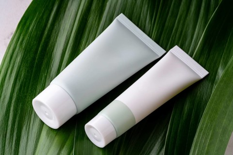 Two minimalist, white and green cosmetic bottles rest on the glossy surface of a vibrant green