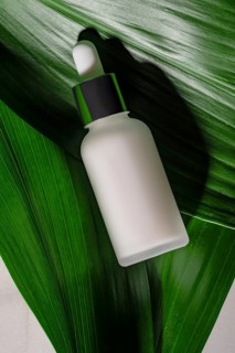 A sleek white cosmetic bottle with a green dropper nestled among fresh green leaves, symbolizing
