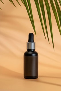 Black cosmetic dropper bottle on a beige background, with palm leaf shadows. The minimalist,