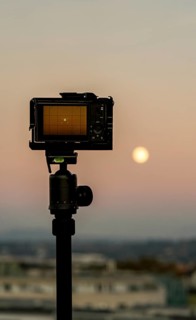 A camera on a tripod silhouetted against a warm sunset sky, overlooking the cityscape of Geneva,