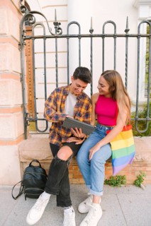 A happy lesbian couple sits outdoors looking at a digital tablet, symbolizing love, equality, and