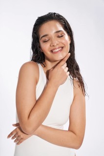 Studio portrait of a joyful female model with wet hair and skin, her eyes gently closed, wearing a