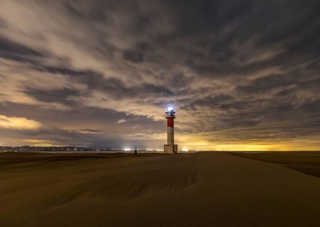 Fangar Lighthouse in Tarragona, Spain stands alone on sandy dunes under a dramatic sky The