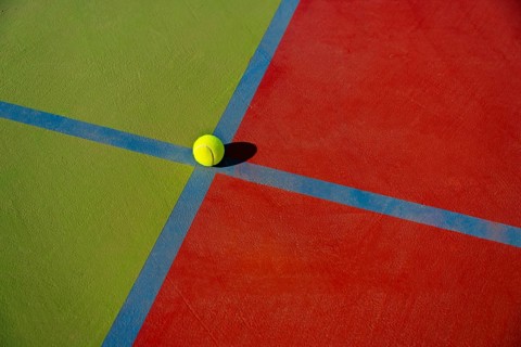 Close-up view of a yellow tennis ball at the intersection of colorful court lines, showcasing the