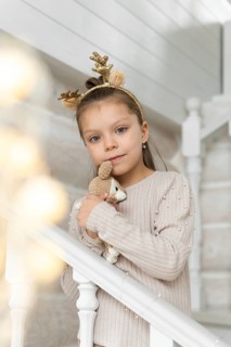 A young girl, dressed in a soft beige sweater adorned with pearls, celebrates Christmas. She wears
