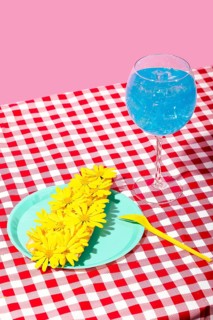 A vibrant summer picnic scene featuring a glass of iced blue beverage and a plate with yellow