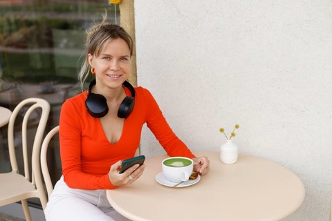 Smiling woman in a bright orange top sits at a Warsaw cafe table She wears headphones around her