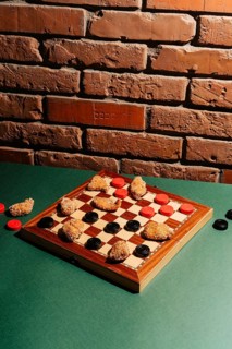 A checkers board on a green surface features chicken nuggets as game pieces. Set against a rustic