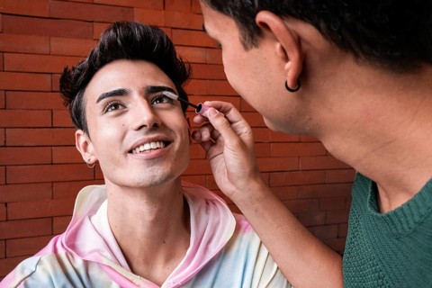 A loving couple, with one applying makeup to the other's lashes. Their joyful expressions and soft