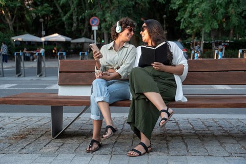 A lesbian couple enjoying a sunny park day. One listens to music with headphones and holds a phone,