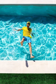 A joyful person in a colorful outfit splashes into a clear blue pool on a sunny day, expressing fun