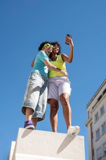 A joyful, multiethnic LGBTQ+ couple captures a selfie outdoors. They stand closely on a sunny day,
