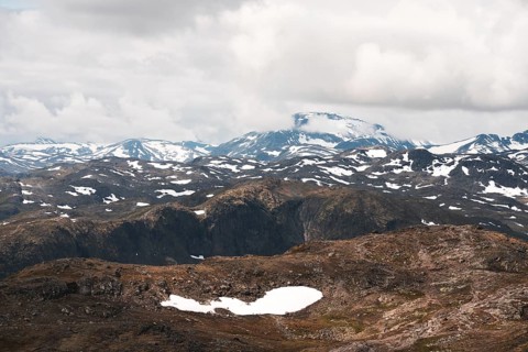 A stunning view of Norway's rugged mountains, dotted with patches of snow The dramatic clouds and