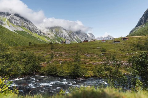 A serene mountain village nestled in a lush green valley in Norway, surrounded by towering peaks