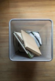 Aerial shot of a metal mesh waste bin containing discarded books, placed on a wooden floor. The