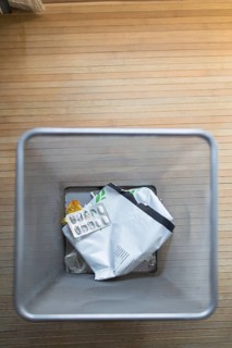A top down view of a trash bin containing used pill packaging and other waste, set on a wooden