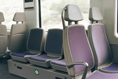 A row of empty train seats with purple upholstery and patterned design by a window. The setting
