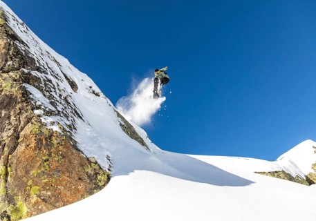 A snowboarder performs an impressive jump off a snow covered mountain, leaving a trail of snow