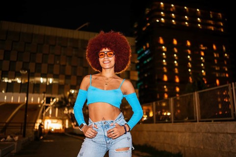 African descendent woman with striking afro hair and sunglasses poses confidently outdoors at night