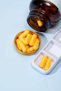 Top view of a dark amber bottle spilling yellow capsules into a gold lid, alongside a white pill