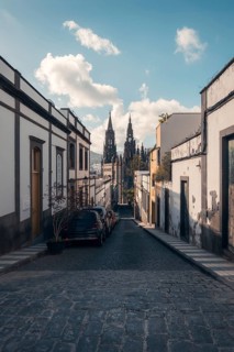 A calm cobblestone street lined with traditional houses leads to the iconic San Juan Bautista