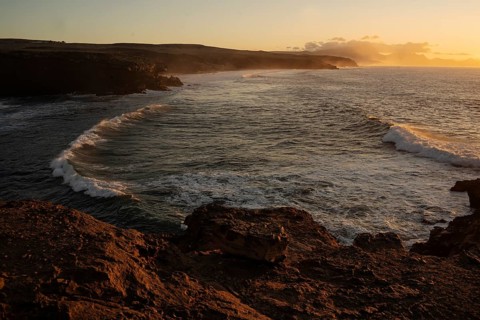 Dramatic view of powerful waves hitting rugged rocks with a sunset backdrop at La Pared,