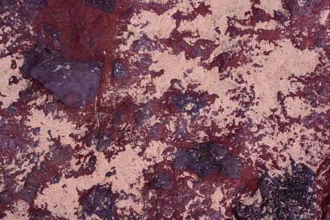Close-up of the intricate textures of volcanic rocks surrounded by scattered sand at La Pared,