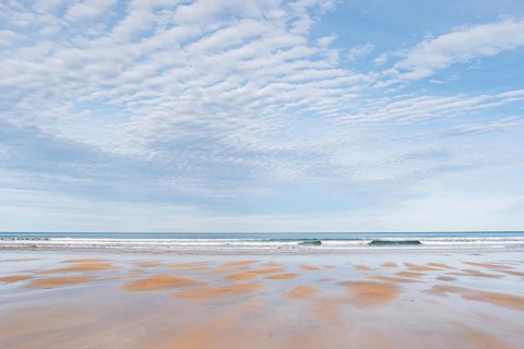 A tranquil beach scene featuring an expansive view of gentle waves under a sky filled with soft