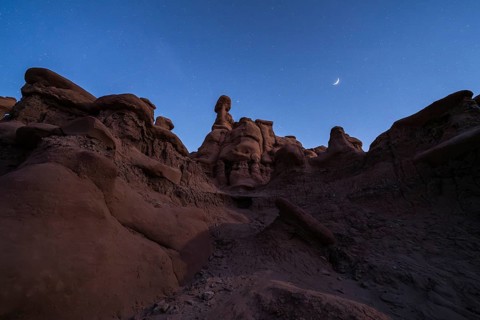 A serene night view of sandstone formations under a starry sky with a crescent moon in Goblin