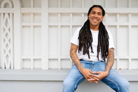 A cheerful man with long dreadlocks and tattoos sits in Barranco, Lima, Peru, exuding a relaxed