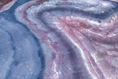 Close up of an sandstone surface, showcasing wavy patterns in pink and blue hues. The intricate