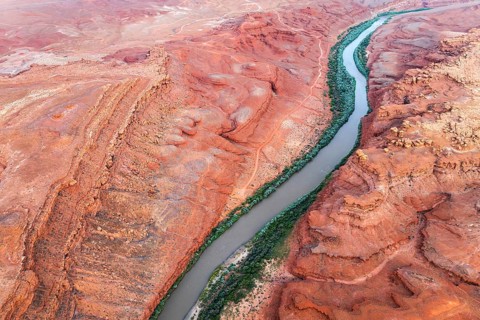 Aerial shot displays the meandering Rio San Juan snaking through vibrant red, rocky terrains of