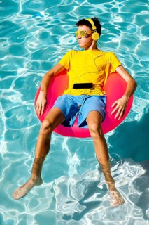 A young teenage boy in vibrant summer attire floats on a pink inflatable ring in clear blue pool