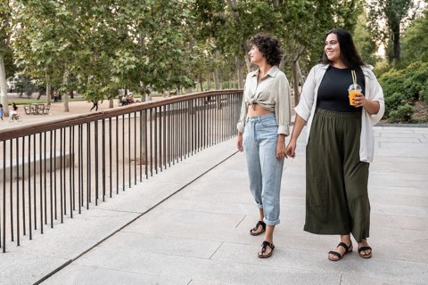A lesbian couple walks hand in hand through a park, enjoying a leisurely stroll. One holds a drink,