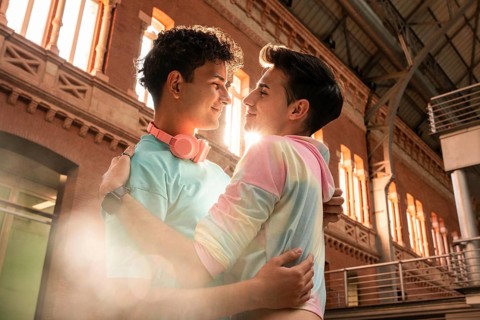 A joyful gay couple embraces lovingly against an urban backdrop, bathed in warm sunlight. The