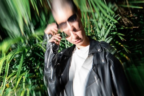 A stylish lesbian woman in a leather jacket and sunglasses is partially blurred against a backdrop