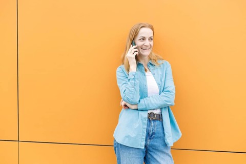 A woman in casual blue and white attire stands against a bright orange wall in Warsaw, Poland,