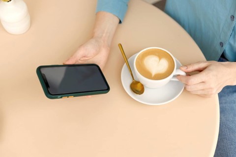 A woman relaxes in a Warsaw cafe, holding a smartphone and a cup of coffee with latte art The cozy