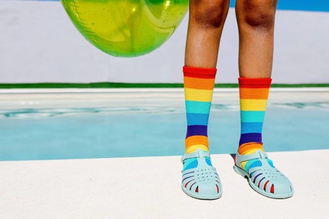 Vibrant rainbow socks and turquoise sandals by a pool, capturing summer's essence. The bright