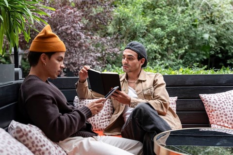 A Colombian gay couple enjoys a quiet day outdoors on a cozy bench. One reads from a book, while