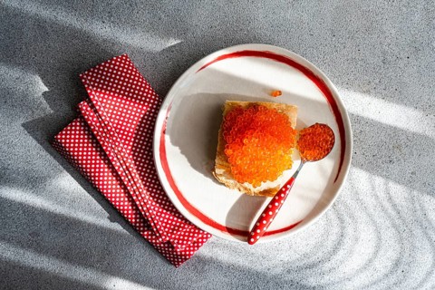 Top view of a plate with organic red trout caviar spread on a toasted slice of bread, accompanied