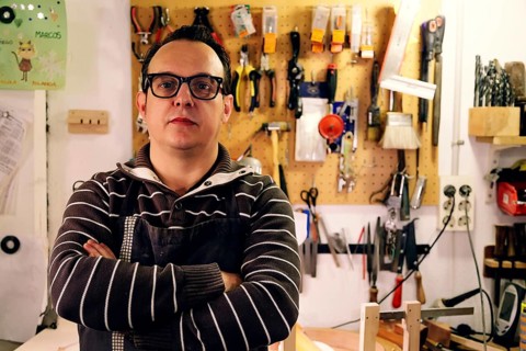 A luthier stands confidently in a bass guitar workshop, surrounded by tools and equipment. The