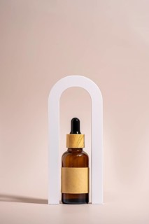 An amber glass dropper bottle with a wooden cap and blank label is elegantly placed in a white arch