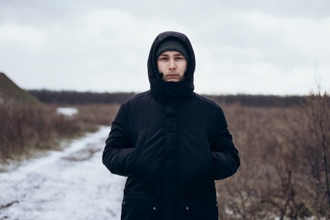 A man walks down a snowy path, dressed warmly in a coat and beanie, enjoying the serene winter