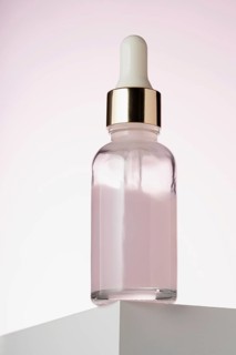 An elegant dropper bottle for cosmetics prominently displayed on a two toned minimalist podium,