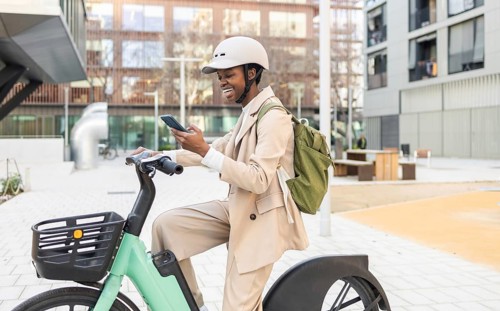 Black woman in a modern urban setting, riding a bicycle and checking her phone Dressed in a light
